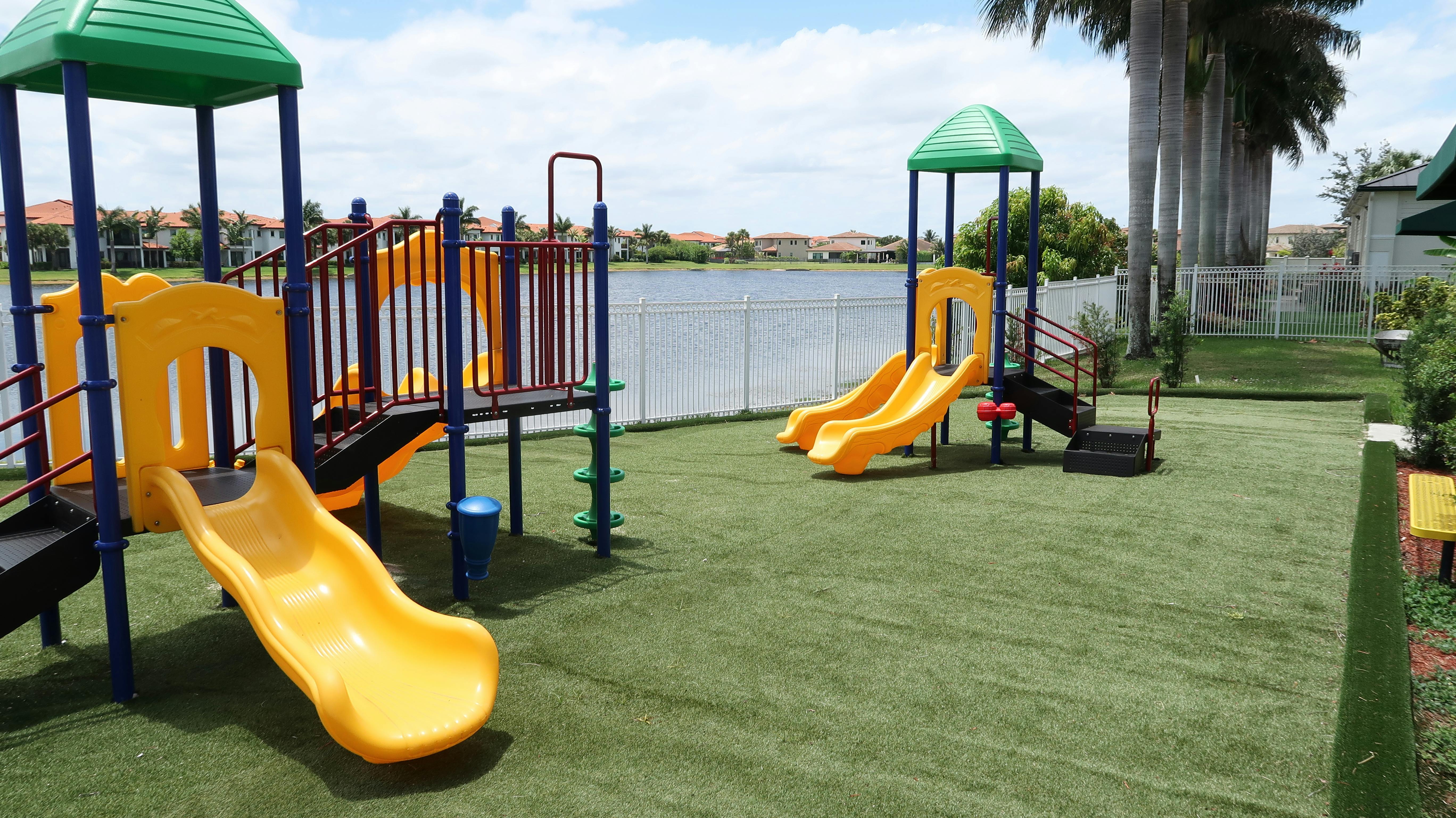 Playground with yellow slides and green roofs on artificial turf next to a lake