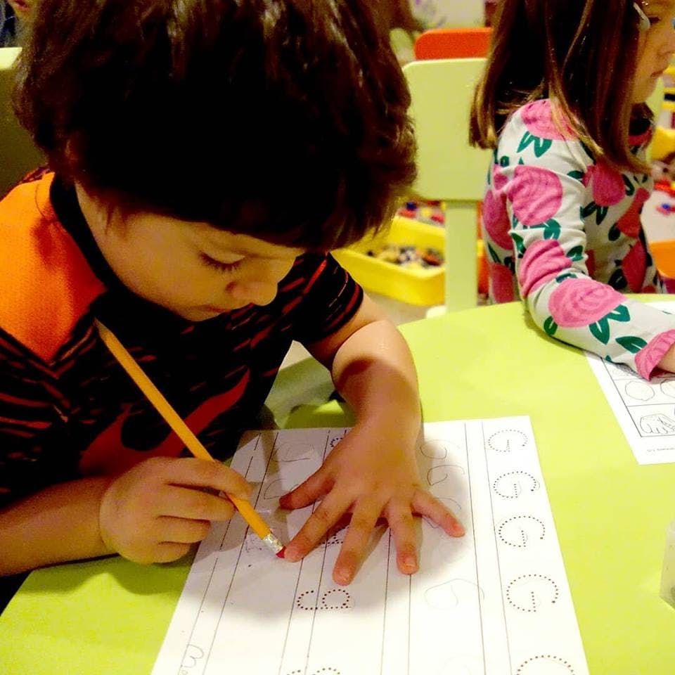 Child writing letters on paper with a pencil