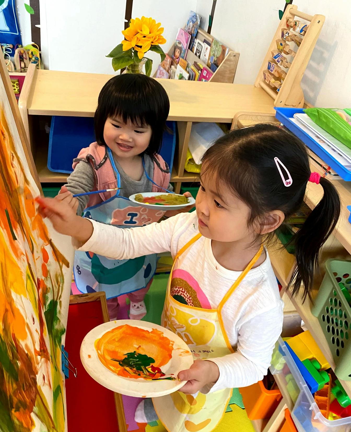 Two children painting on an easel in a classroom