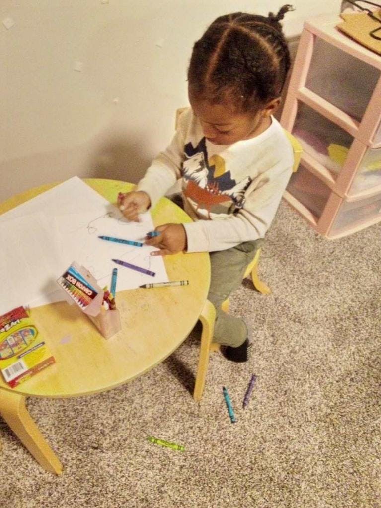 Child drawing with crayons at a small table