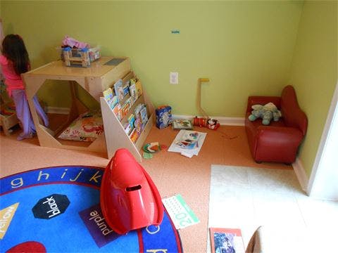 Child standing next to a wooden play structure in a room with toys