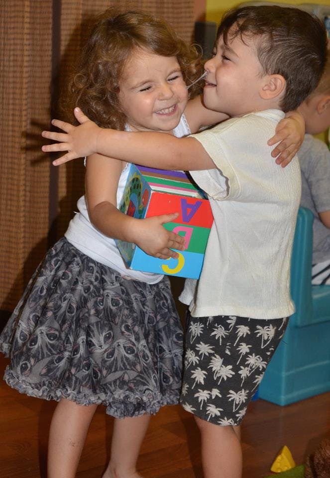 Two children hugging, one holding a colorful block