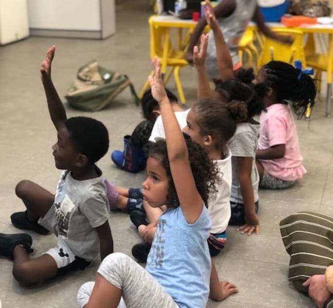 Children sitting on the floor with hands raised in a classroom
