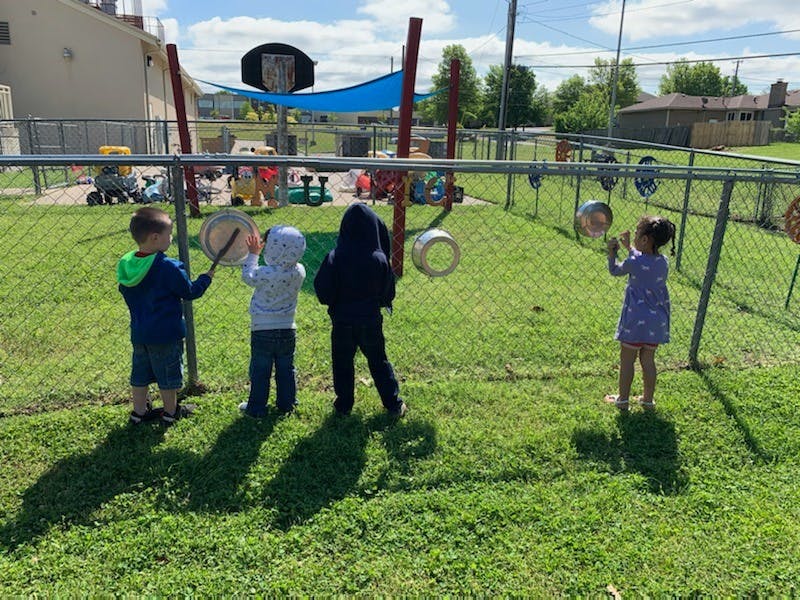 Children playing with pots and pans on a fence