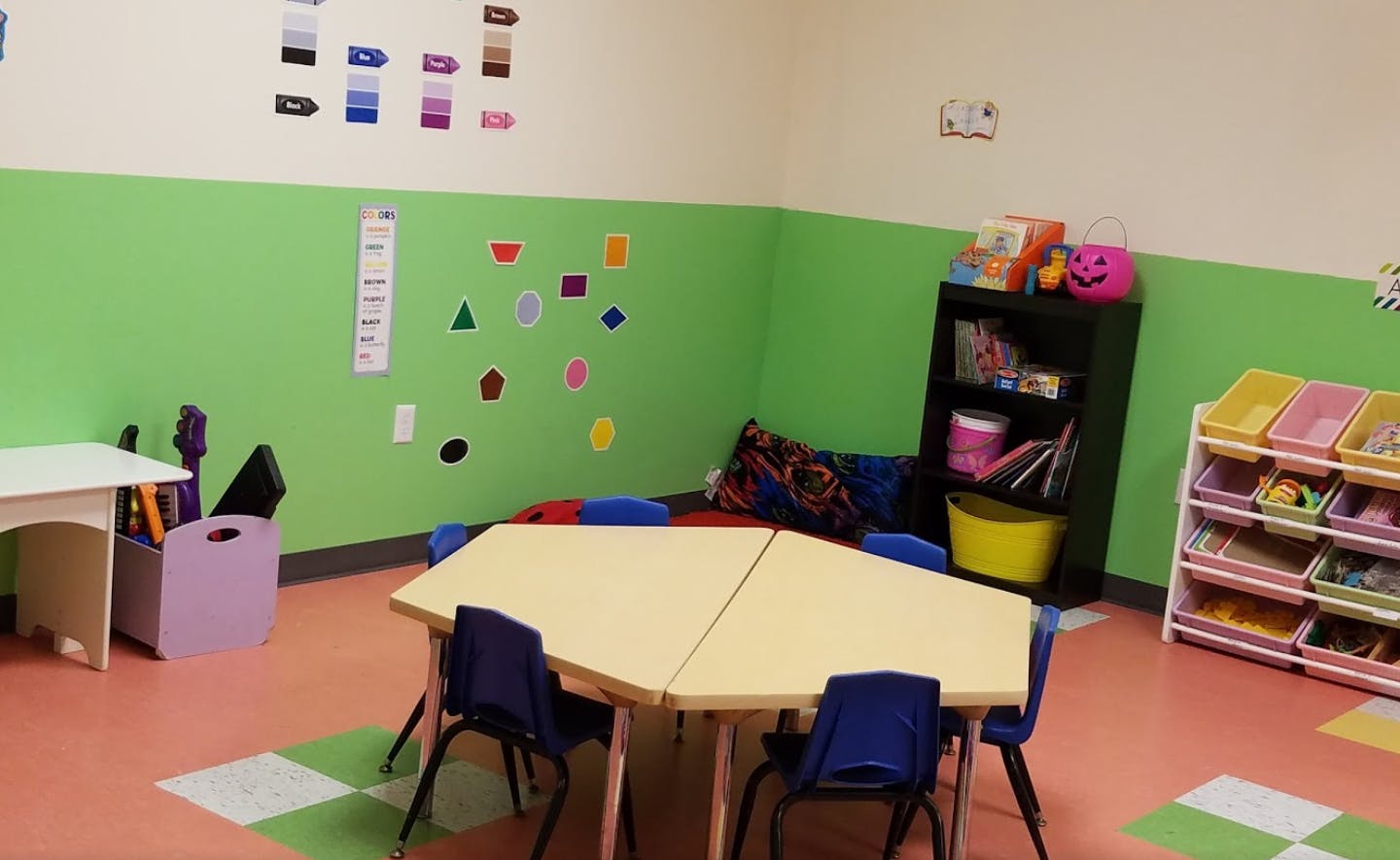Classroom with small tables and chairs, shelves with books and toys