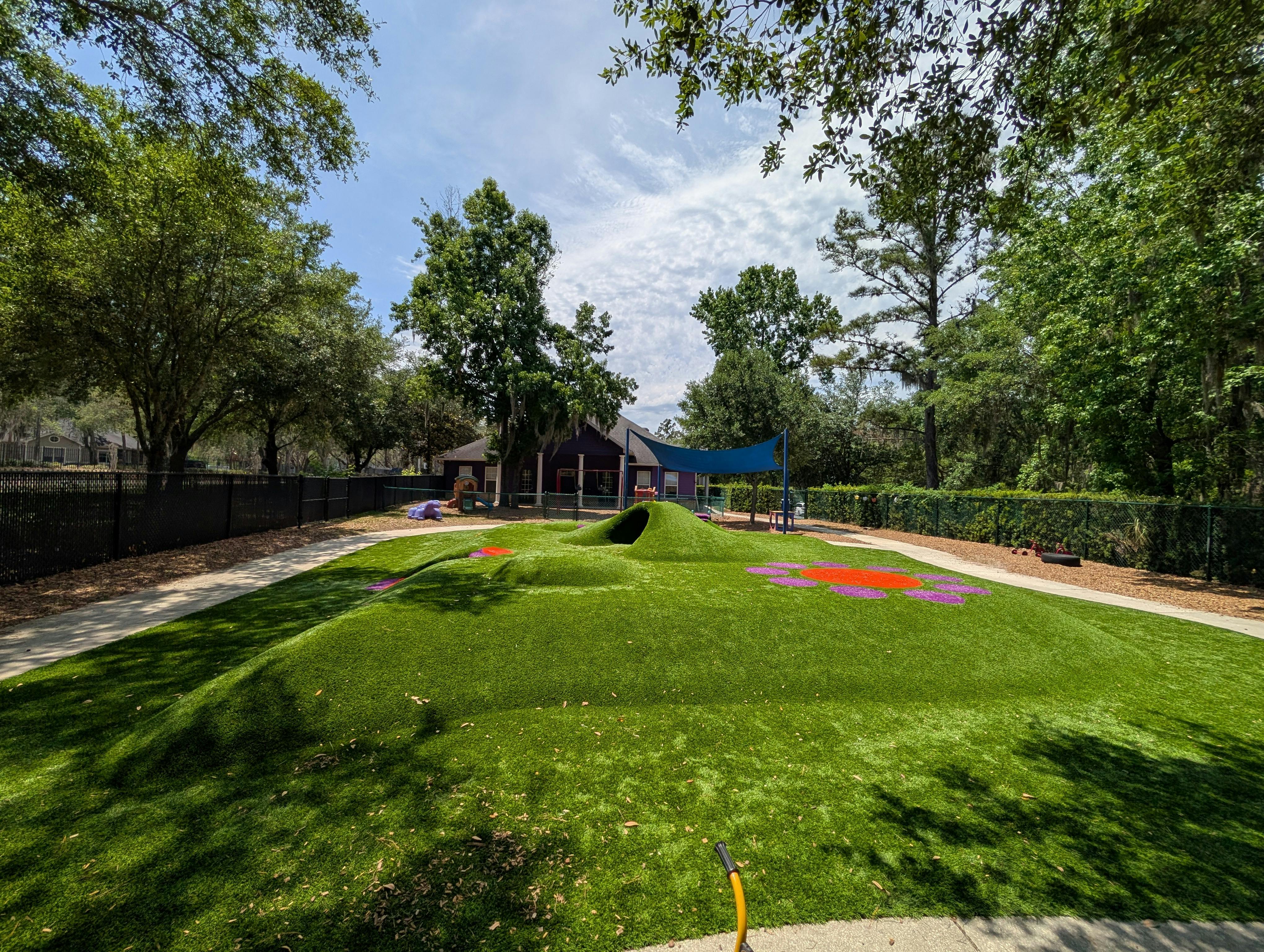 Outdoor playground with green artificial turf hills and a blue shade canopy