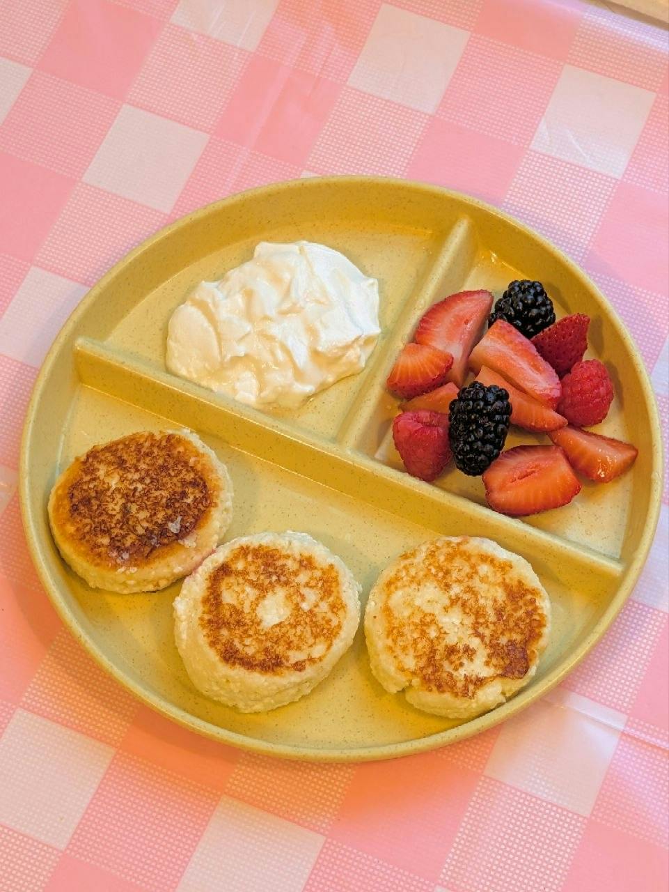Cottage cheese pancakes with fresh berries and yogurt on a divided plate