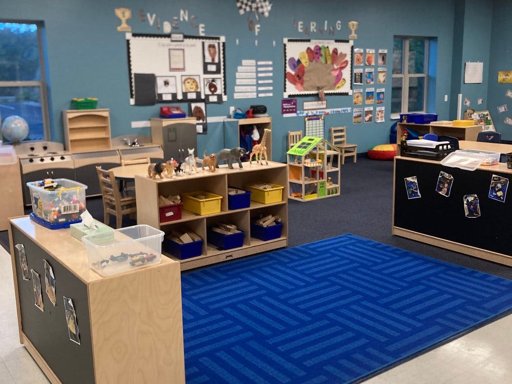Classroom with toy kitchen, animal figurines, blue rug, and educational displays