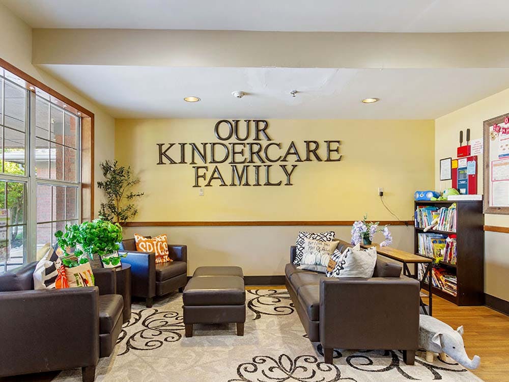 Lobby area with brown couches, armchairs, a rug, and a sign reading "OUR KINDERCARE FAMILY"
