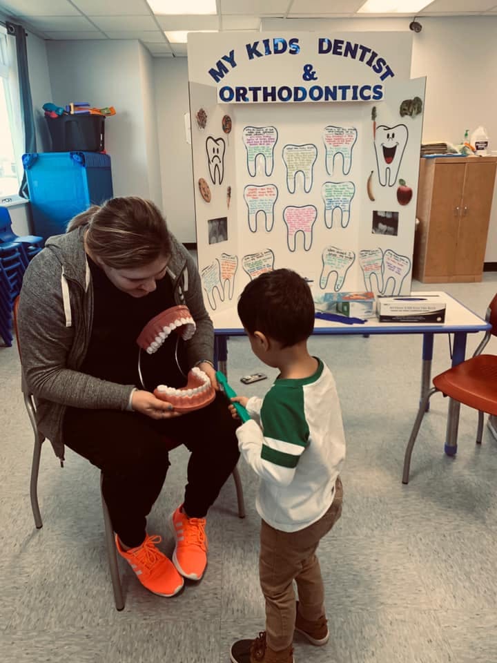 Person holding a large dental model while a child brushes its teeth