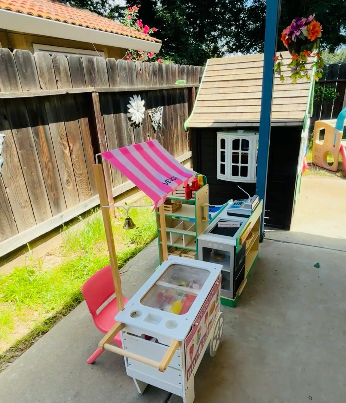 toy ice cream cart with a pink striped awning next to a small playhouse