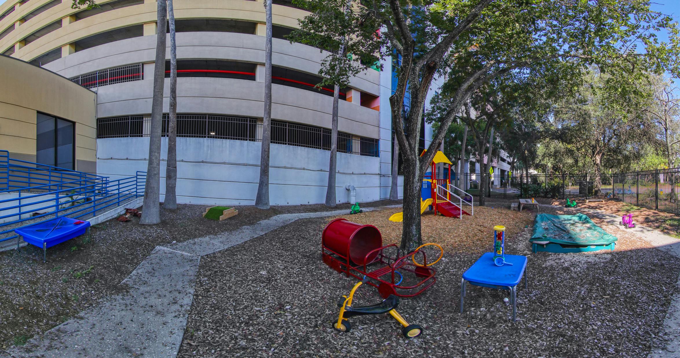 Playground with slide structure, sandboxes, and toy ride-ons next to a parking garage