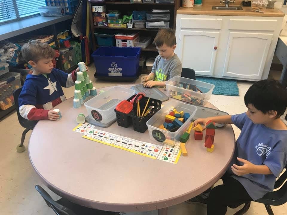 Three children playing with toys at a round table in a classroom
