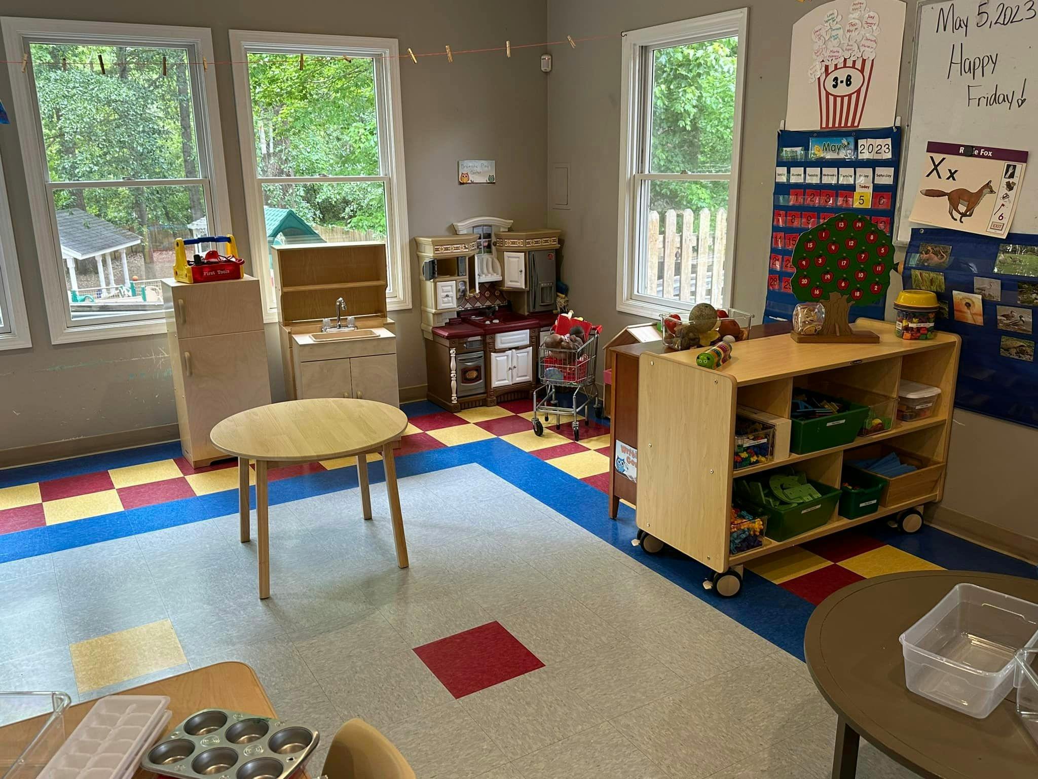 Classroom with small tables, shelves, and play kitchen