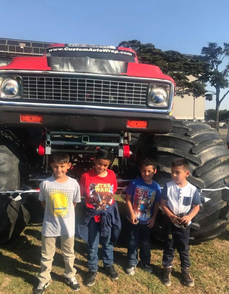 Four children standing in front of a large red monster truck