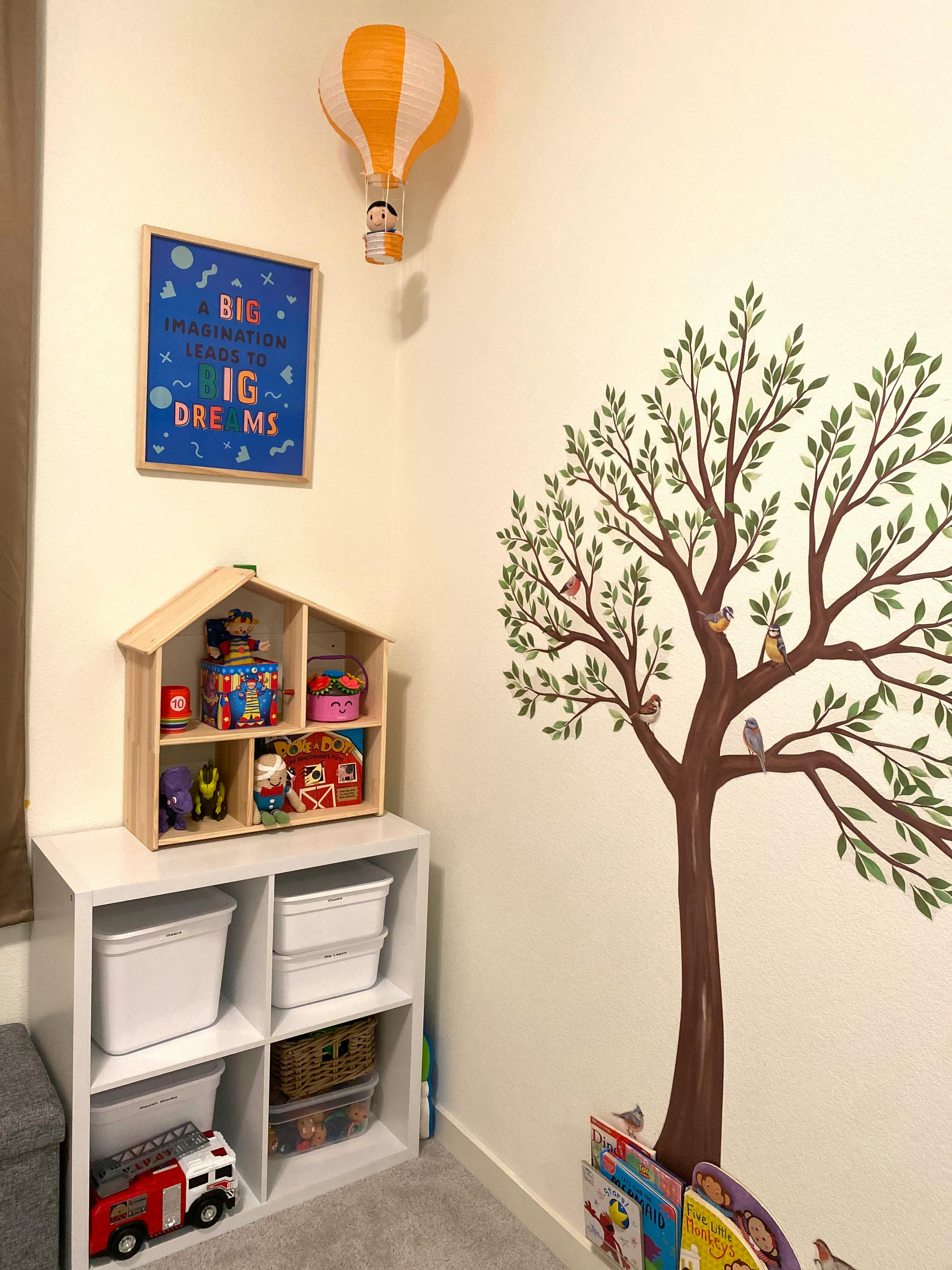 Child's room with a tree wall decal, toy shelf, and hot air balloon decoration