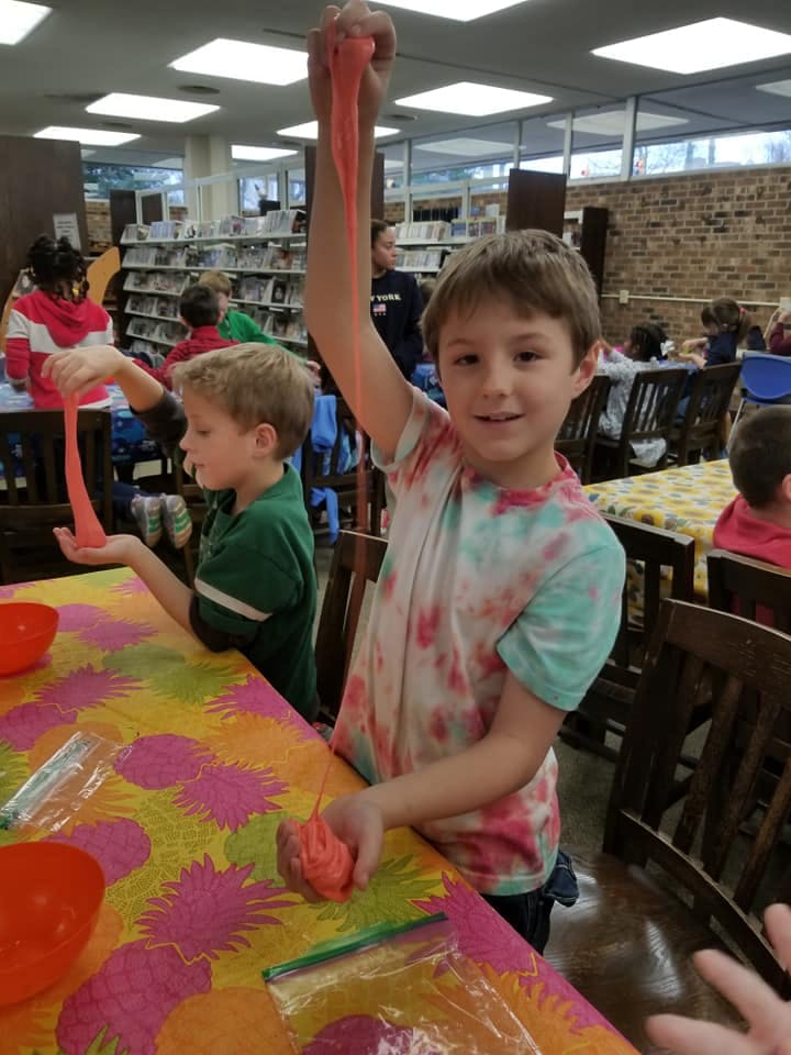 Child holding up orange slime, another child playing with slime at a table
