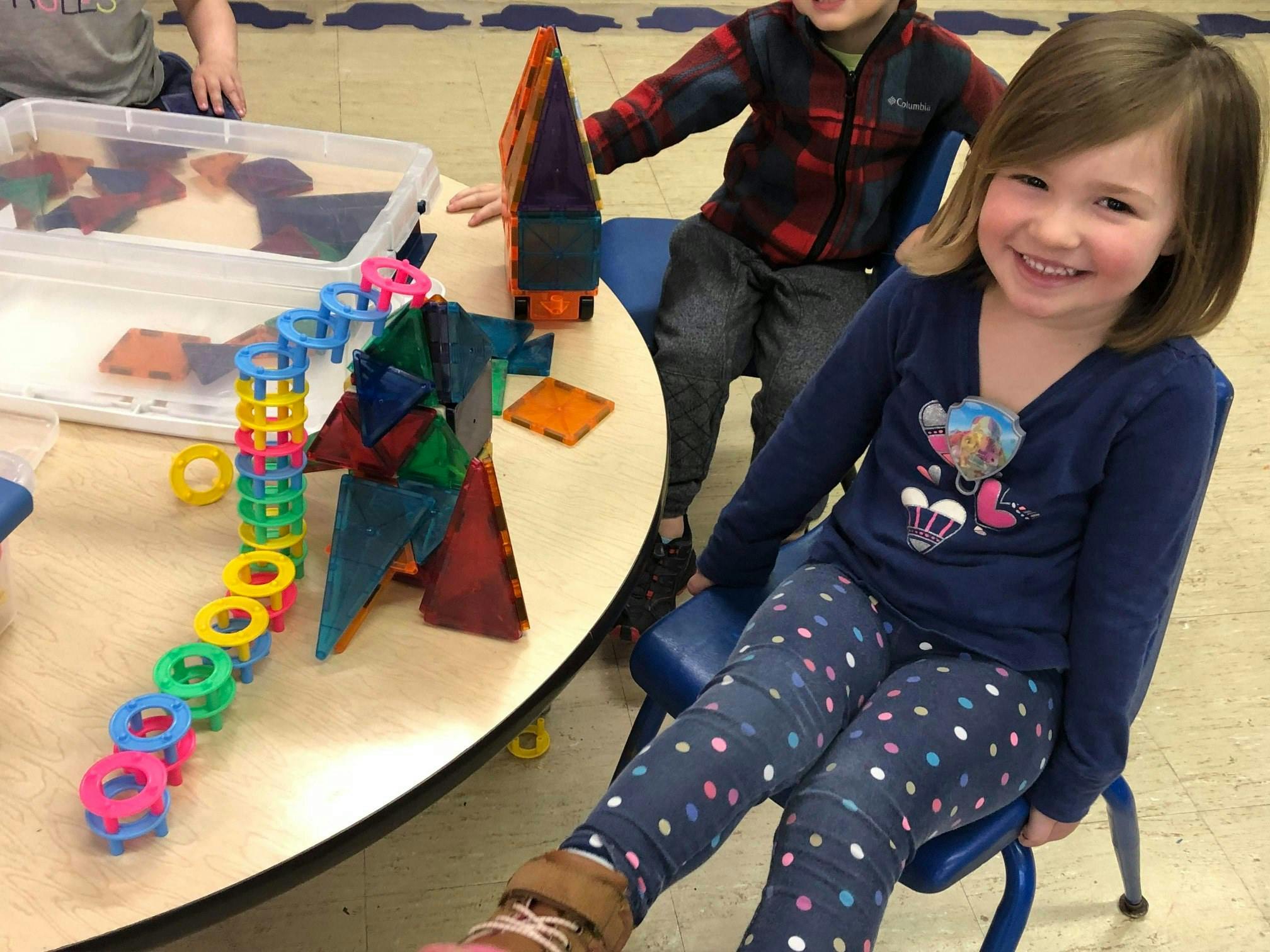Child sitting at a table with magnetic tiles and colorful rings