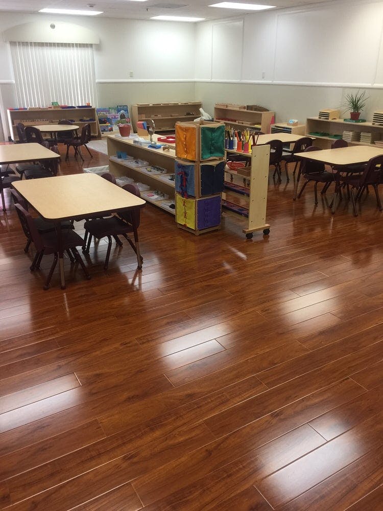 Classroom with small tables and chairs, shelves with learning materials