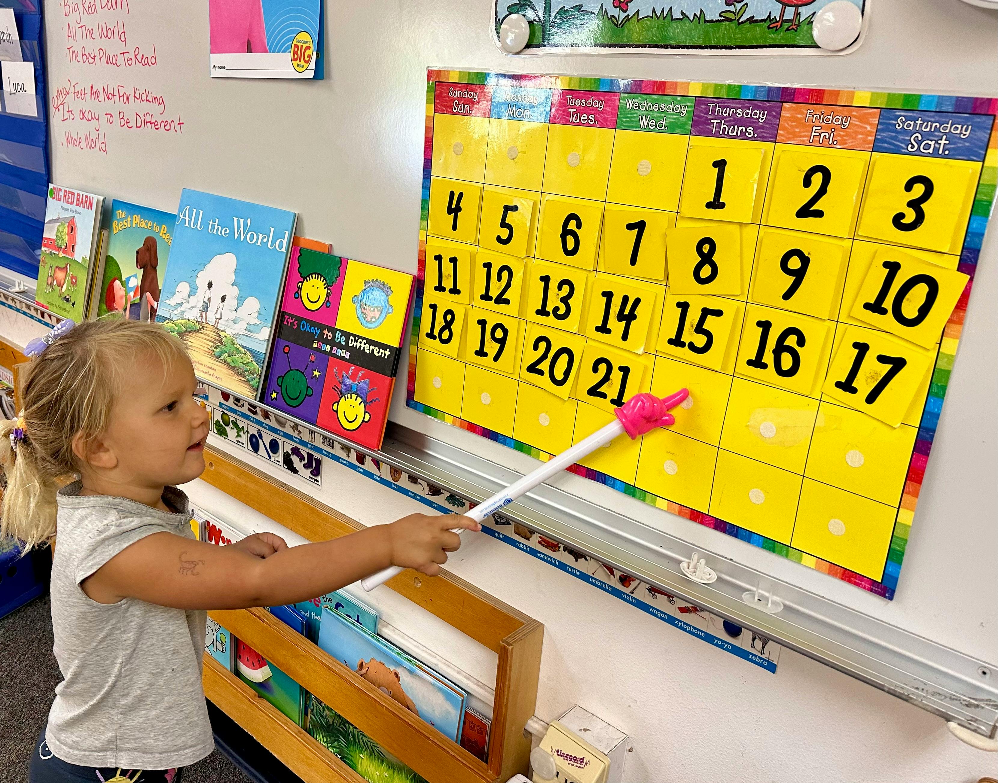 Child pointing to a calendar with a pointer in a classroom
