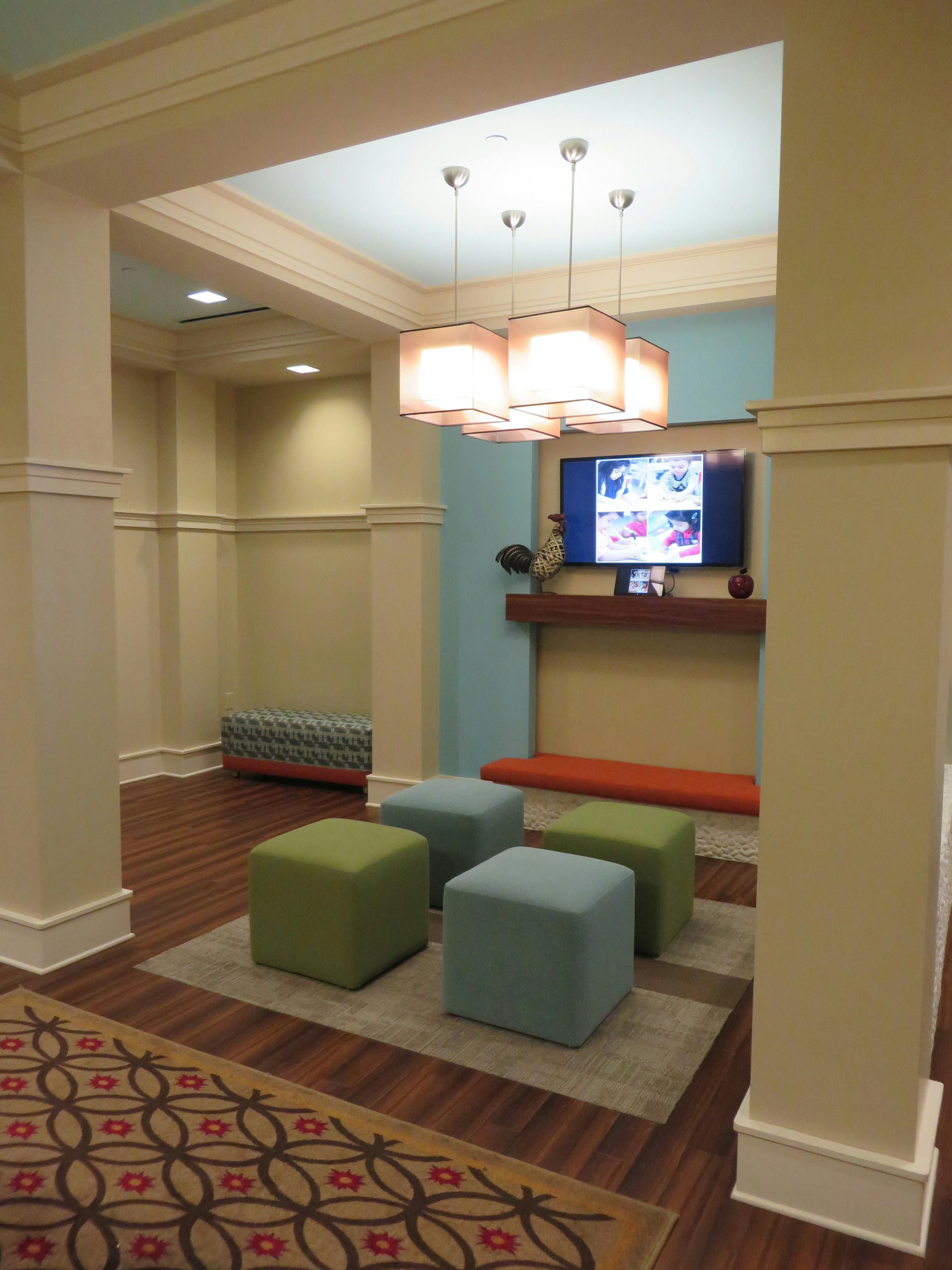 Lounge area with colorful ottomans, a television, and hanging light fixtures