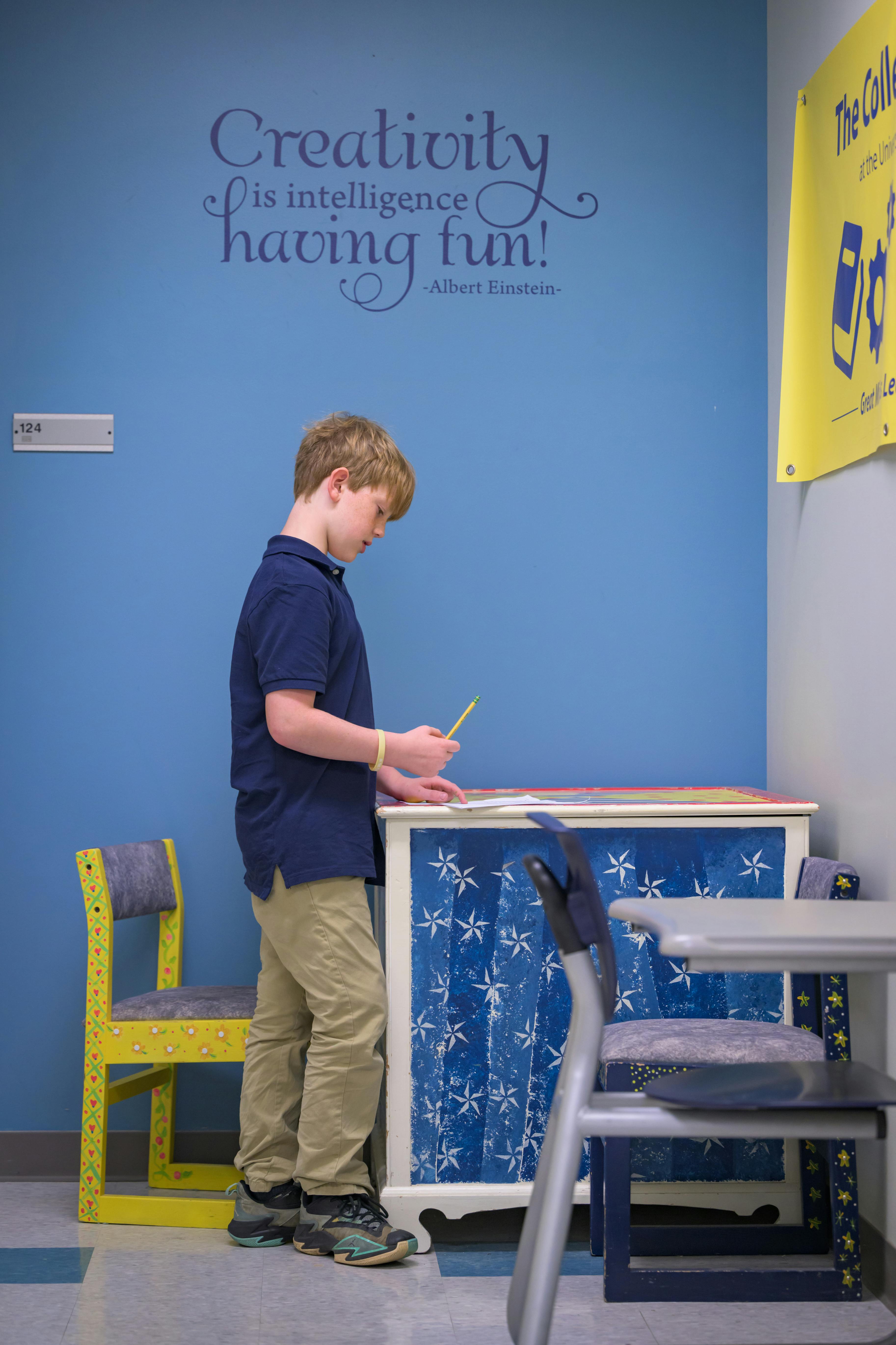 Child standing and writing on a surface in a classroom