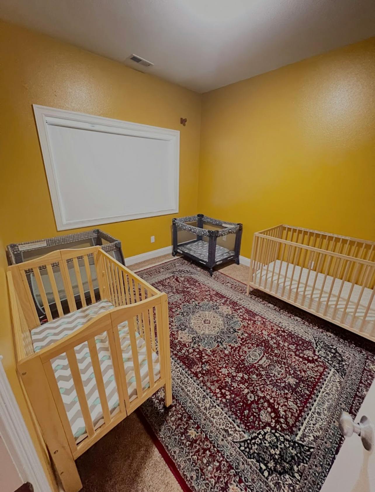 Three cribs in a room with yellow walls and a patterned rug