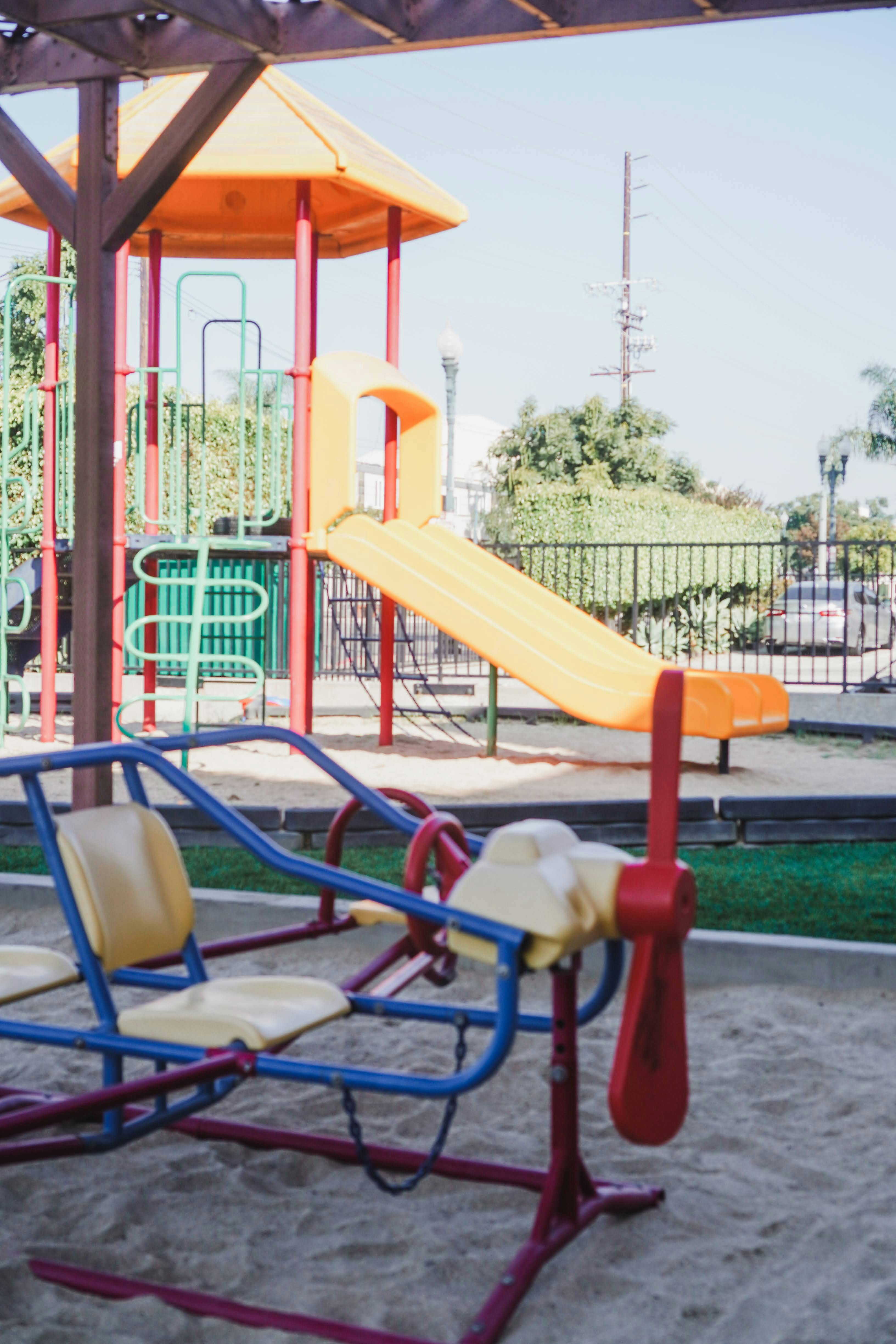 Playground with a yellow slide and a red and blue seesaw in sand