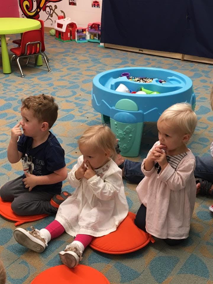 Three children sitting on orange cushions in a classroom