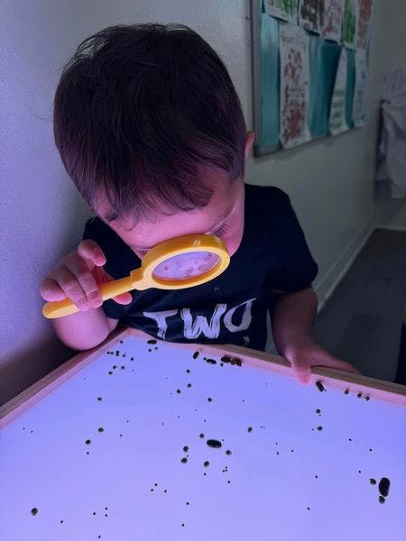 Child looking through a magnifying glass at a light table