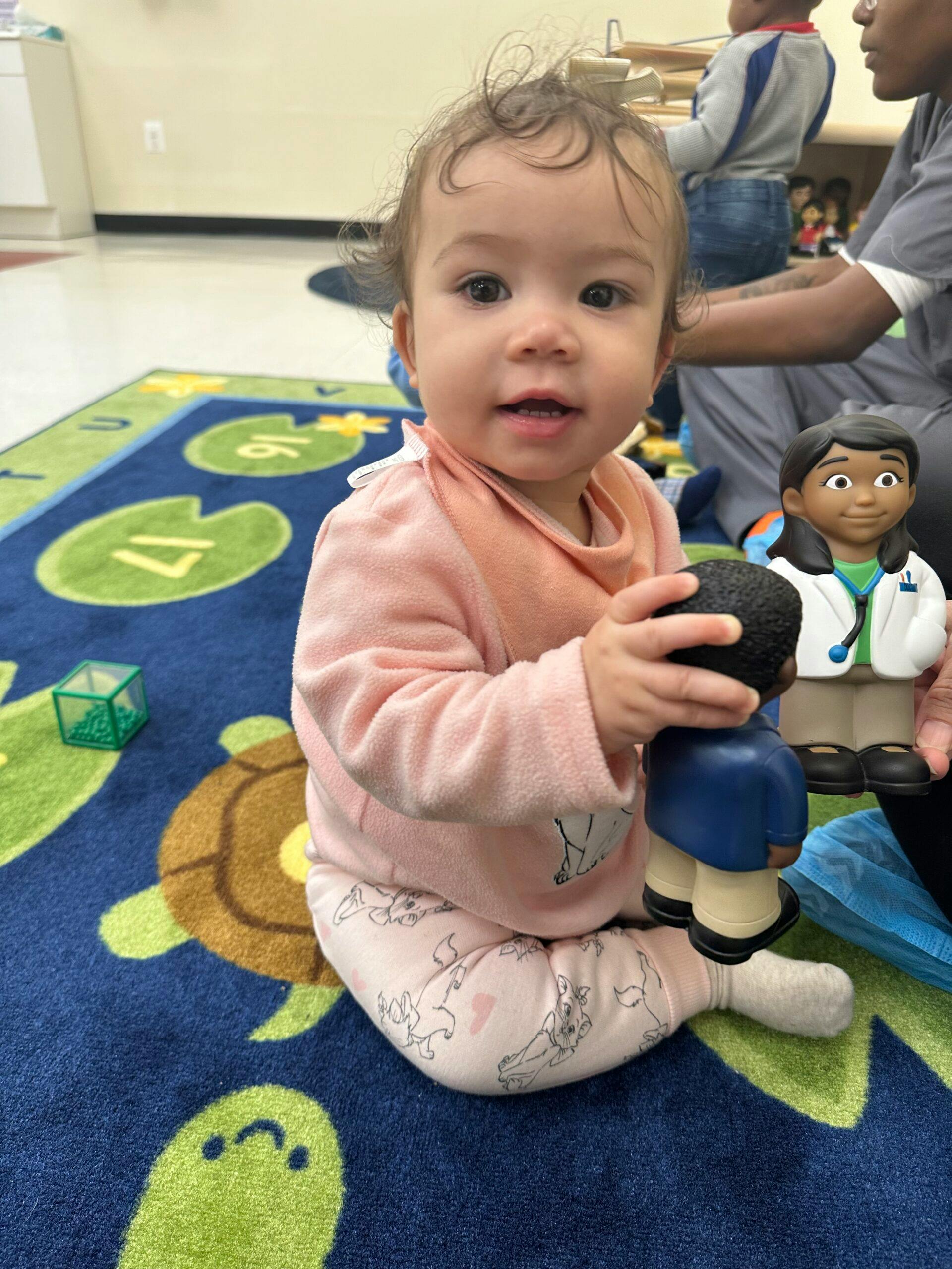 Child on a turtle-patterned rug holding two doctor dolls