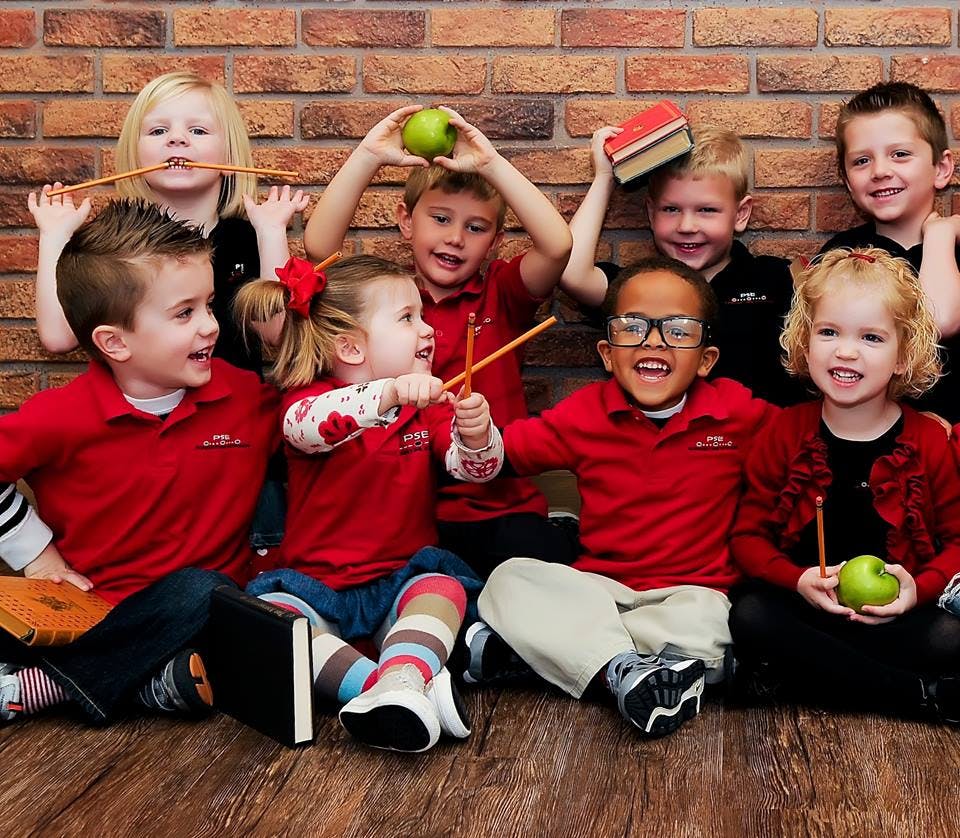 Group of children sitting on the floor, some holding apples or books