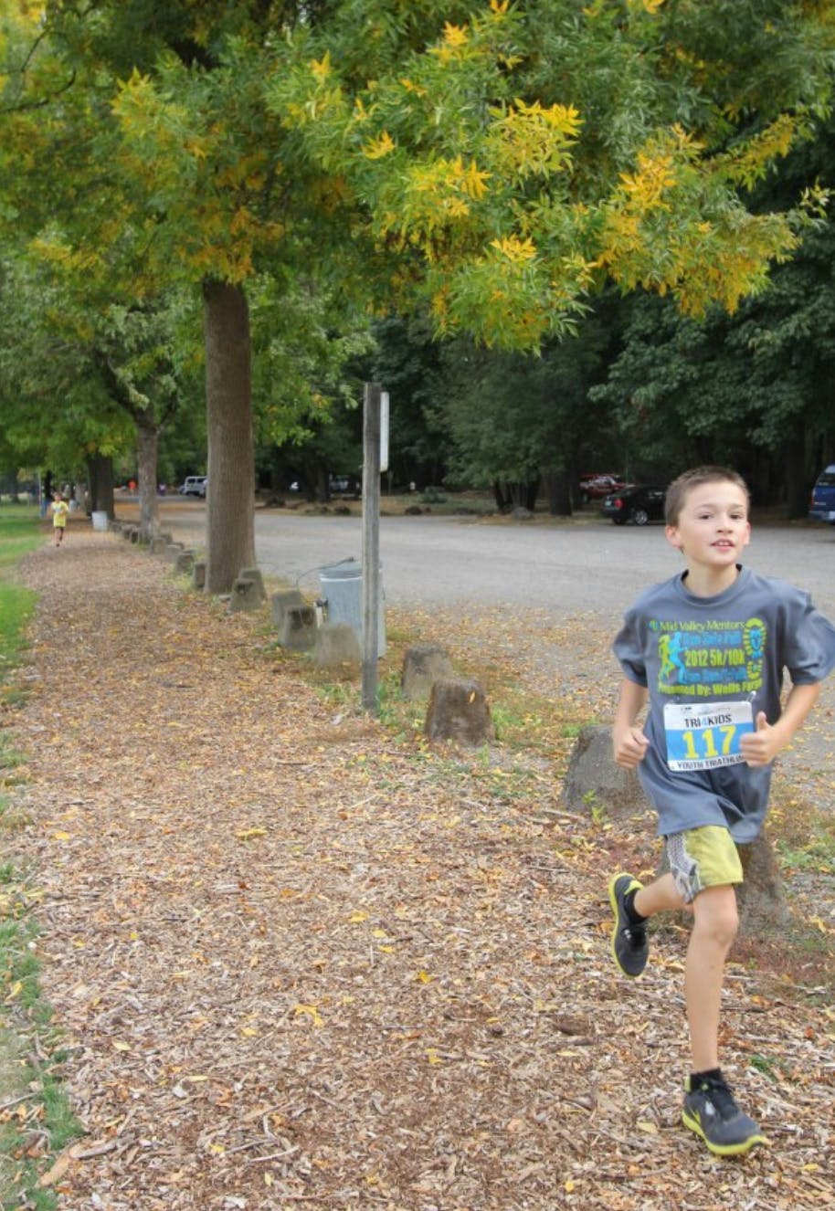 Child running on a wood chip path with a race bib