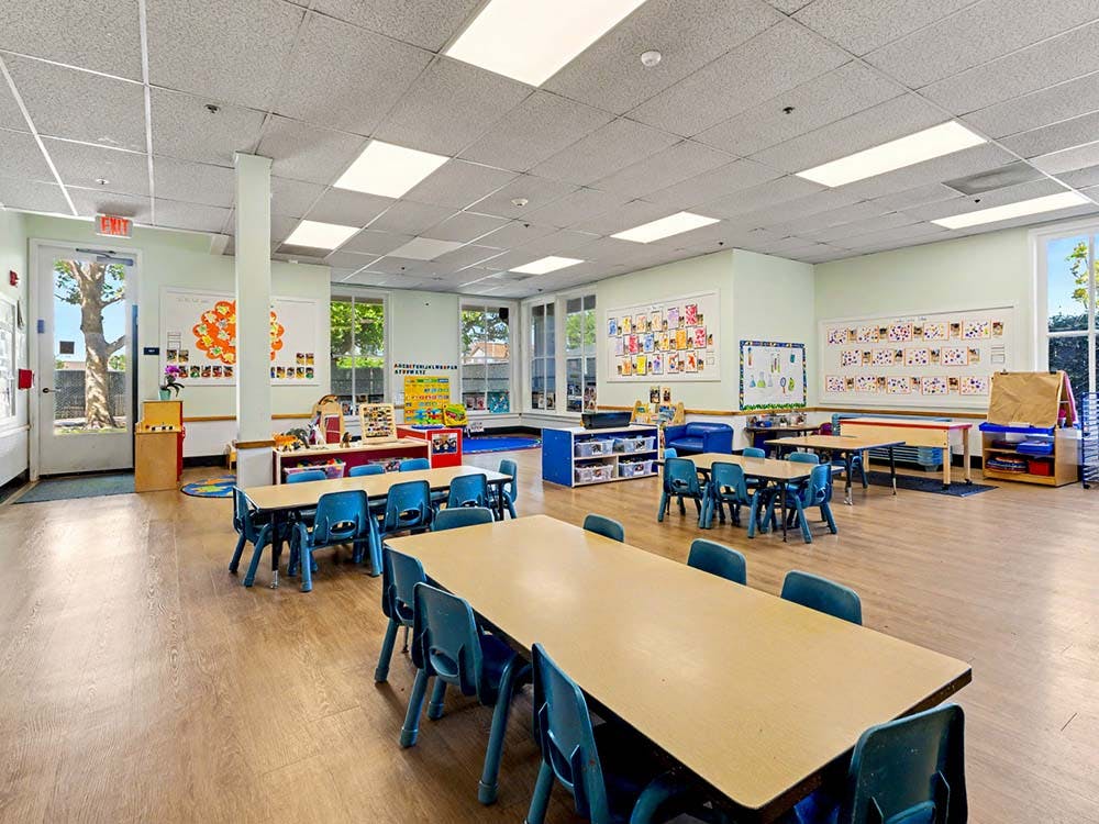 Empty classroom with small tables and chairs, artwork on walls