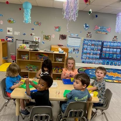 Group of children playing with playdough at a table in a classroom