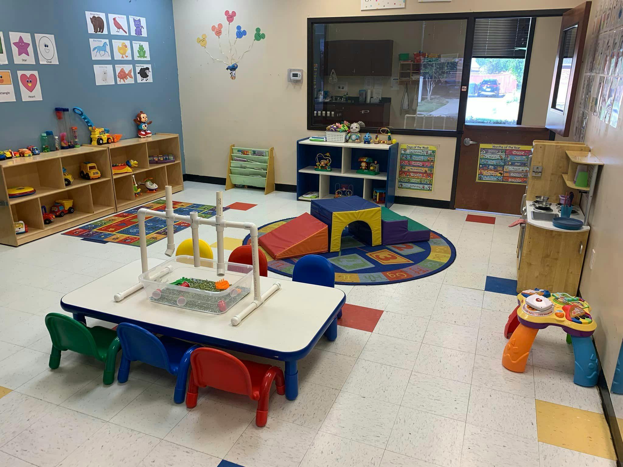 Playroom with small tables and chairs, shelves of toys, and a soft play area