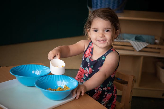 Child pouring from a measuring cup into a blue bowl