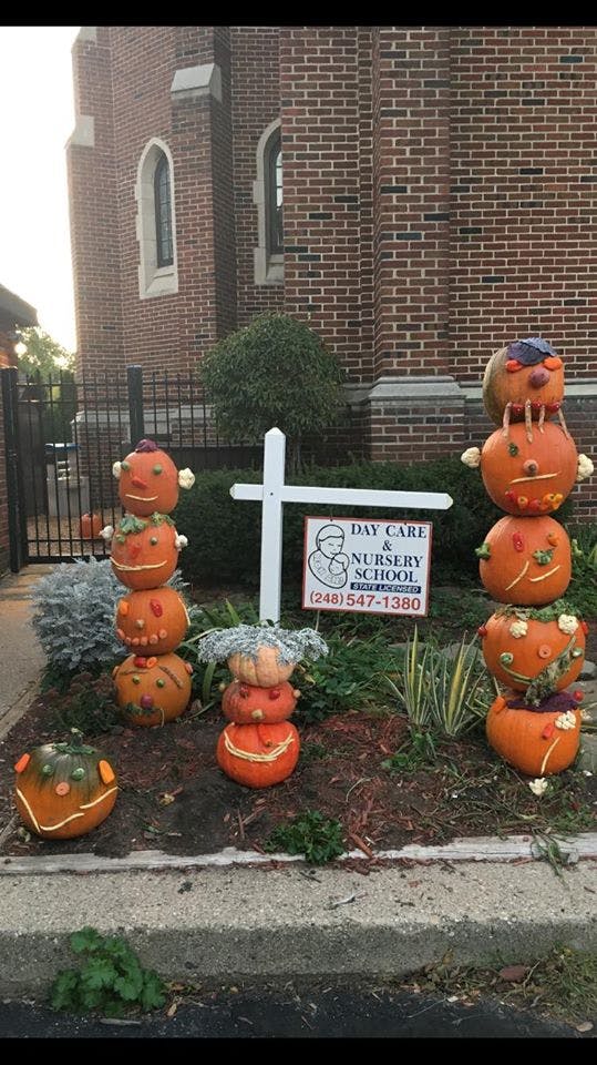 Decorated pumpkins stacked in a garden bed with a sign for a day care and nursery school