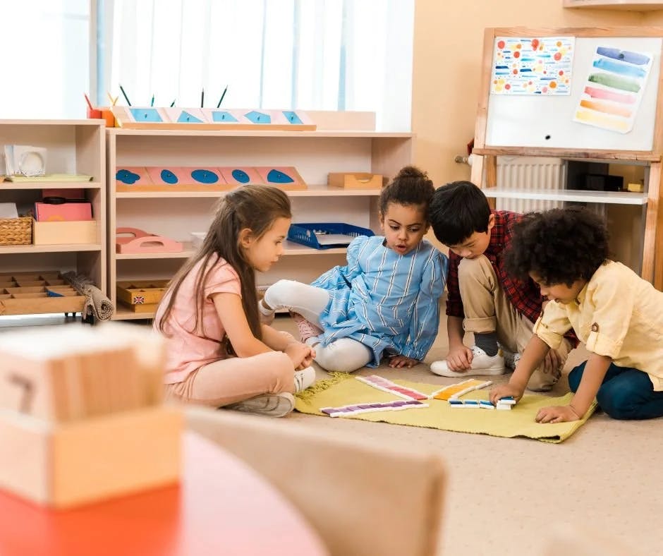 Four children sitting on the floor in a classroom playing with colorful blocks