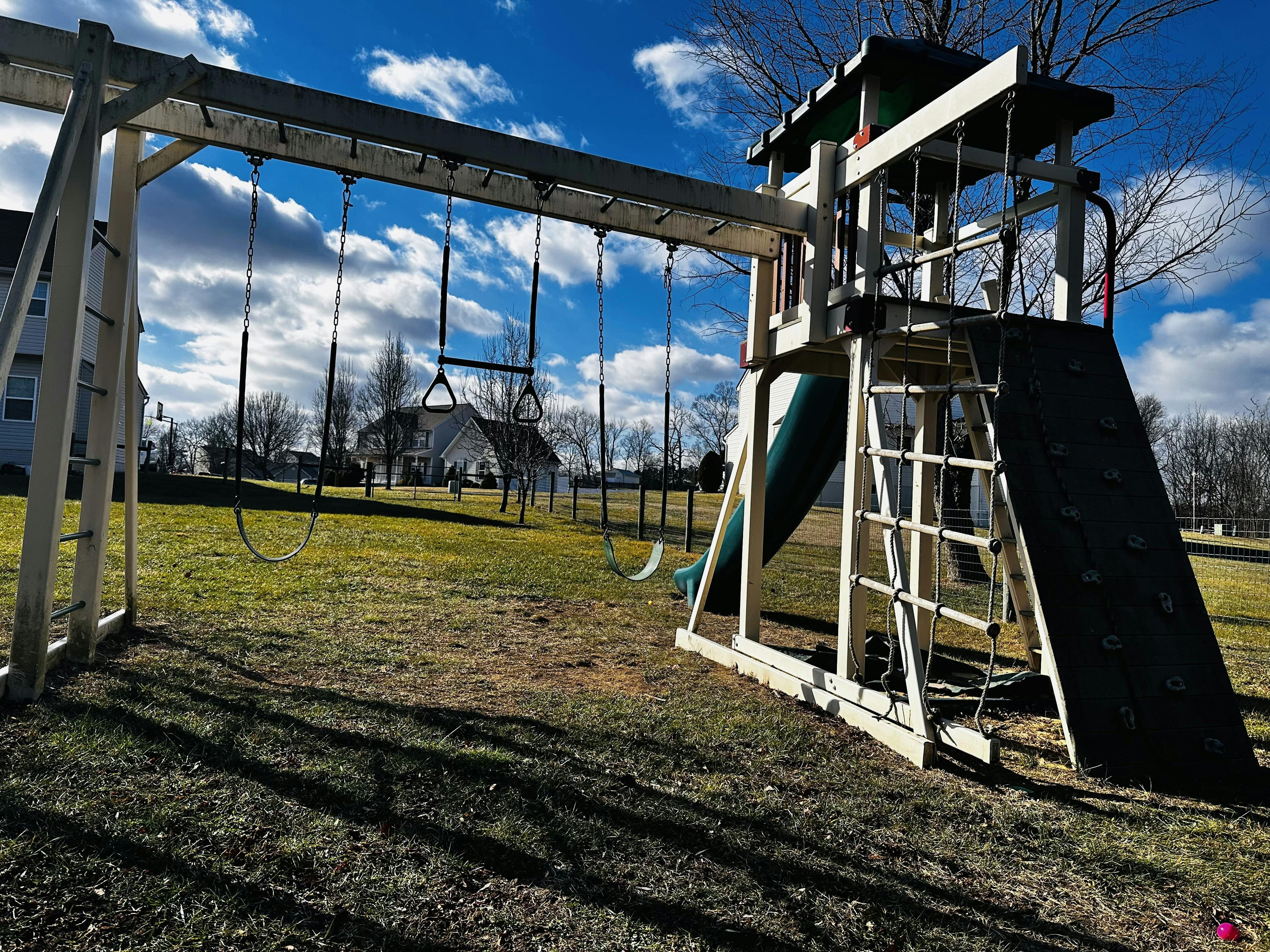 Wooden playground set with swings, slide, and climbing wall