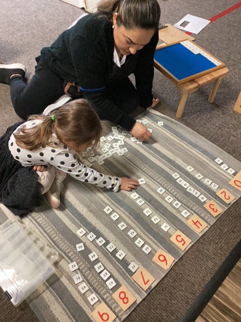 Adult and child arranging number tiles on a striped mat