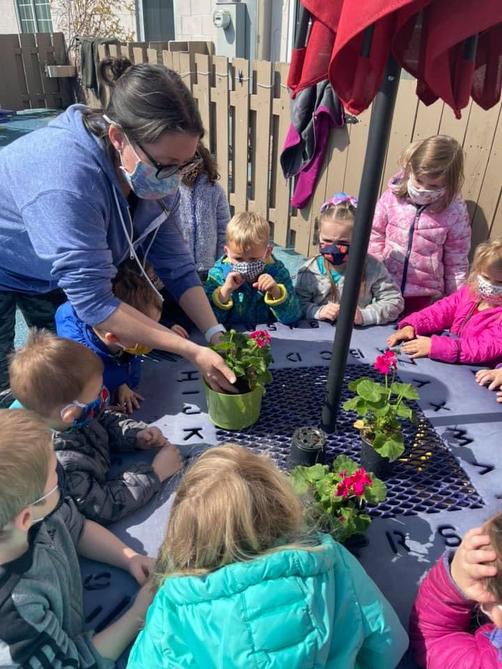 Adult and children planting flowers at a table outdoors