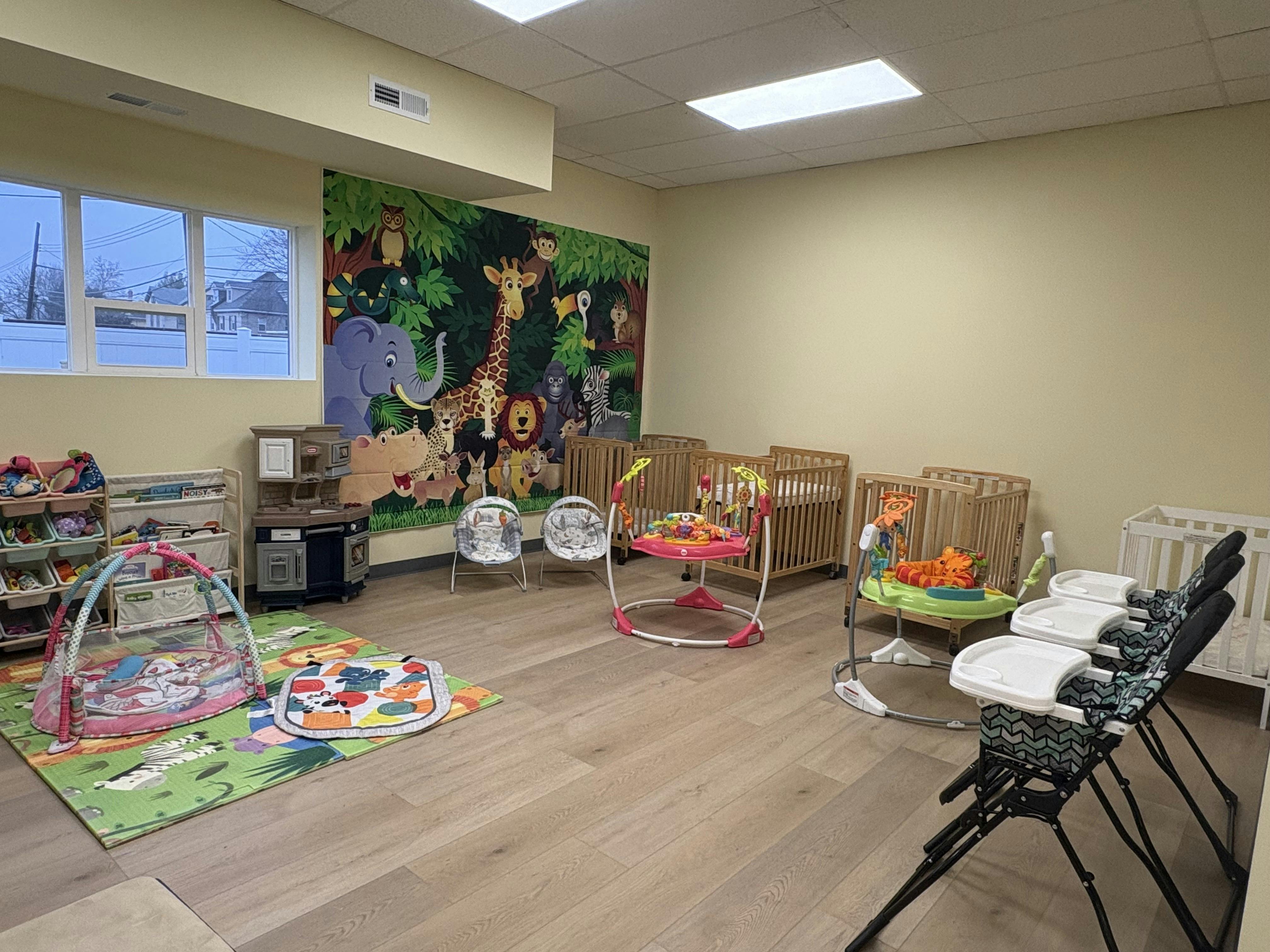 A colorful childcare room with cribs, play mats, and activity chairs