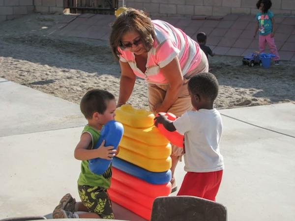 Person and two children playing with a large stacking toy outdoors