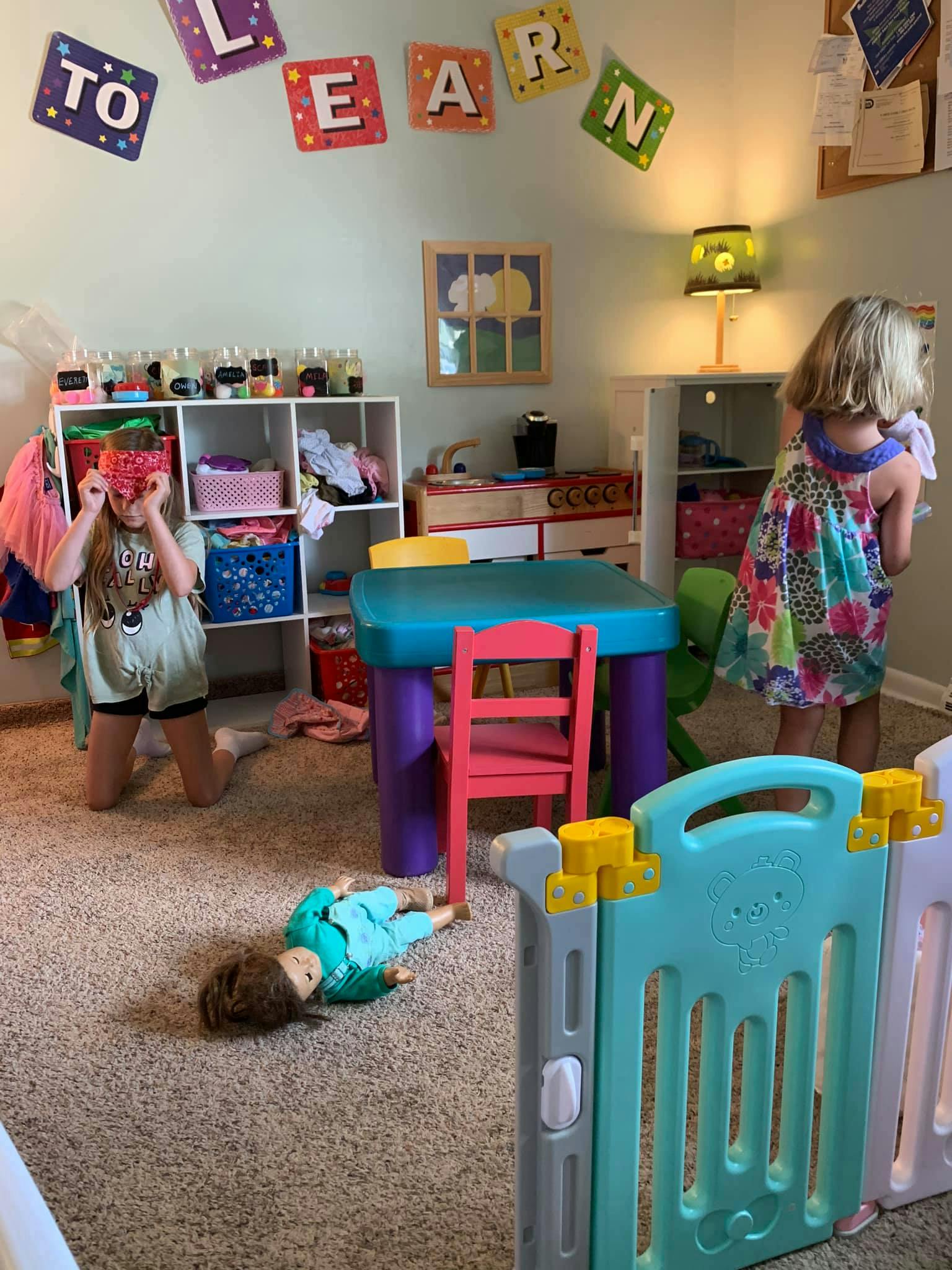 Child kneeling with hands to face, child standing, and doll on floor in playroom