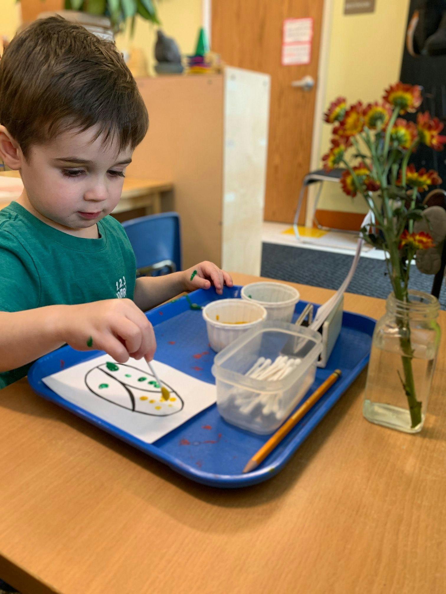 Child painting a drawing on a blue tray