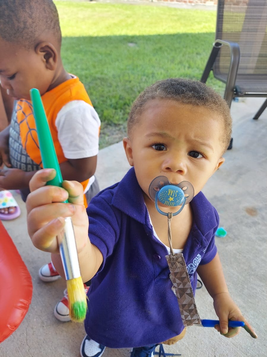 Child with a pacifier holding a paintbrush