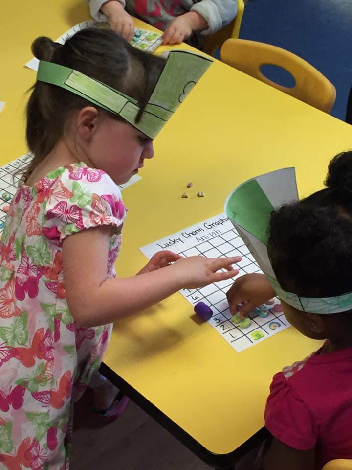 Two children at a yellow table working on a grid activity