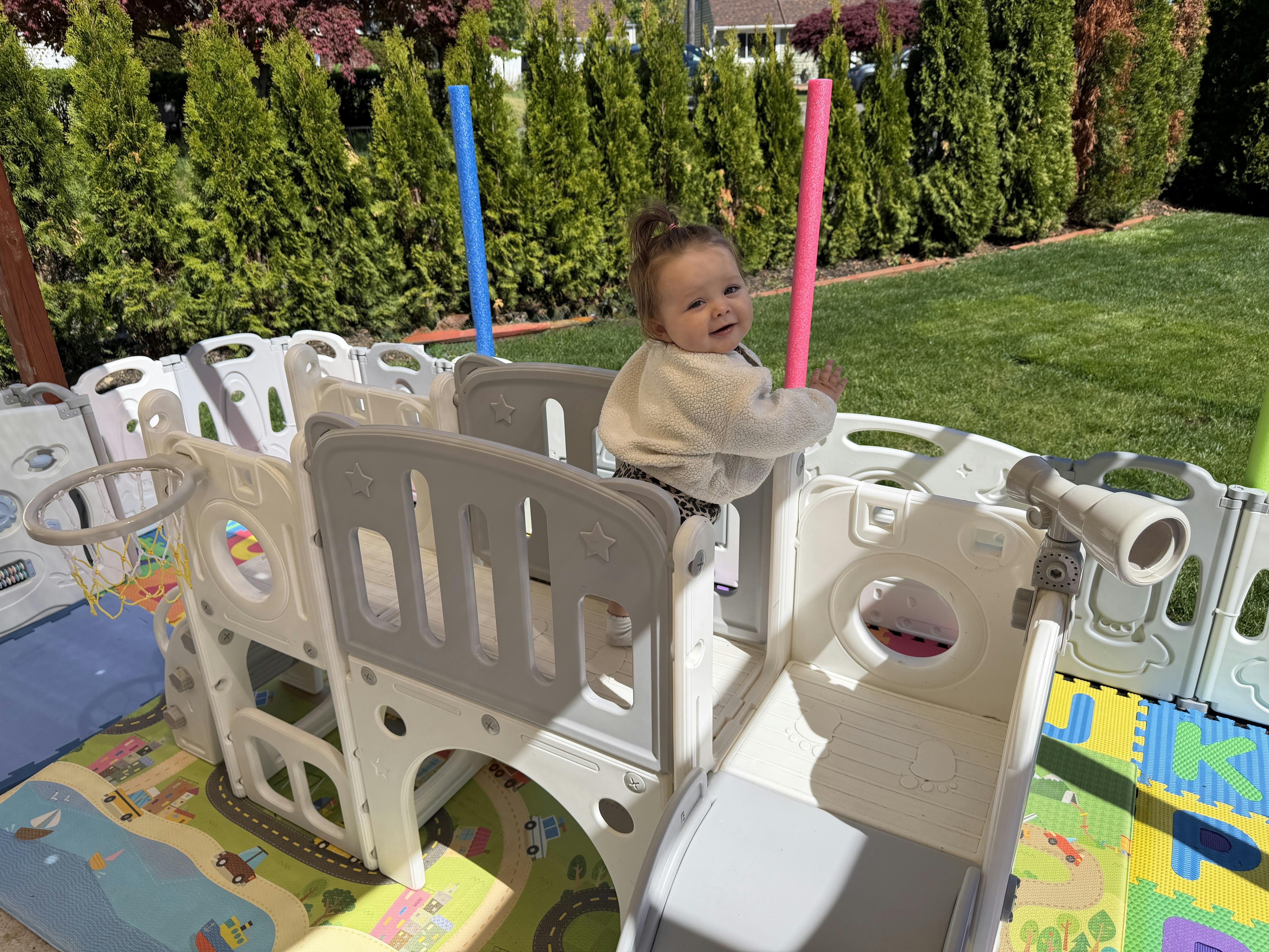 child in a cream-colored play structure with a pink pool noodle