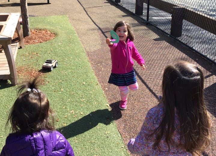 Child holding up a green object to another child